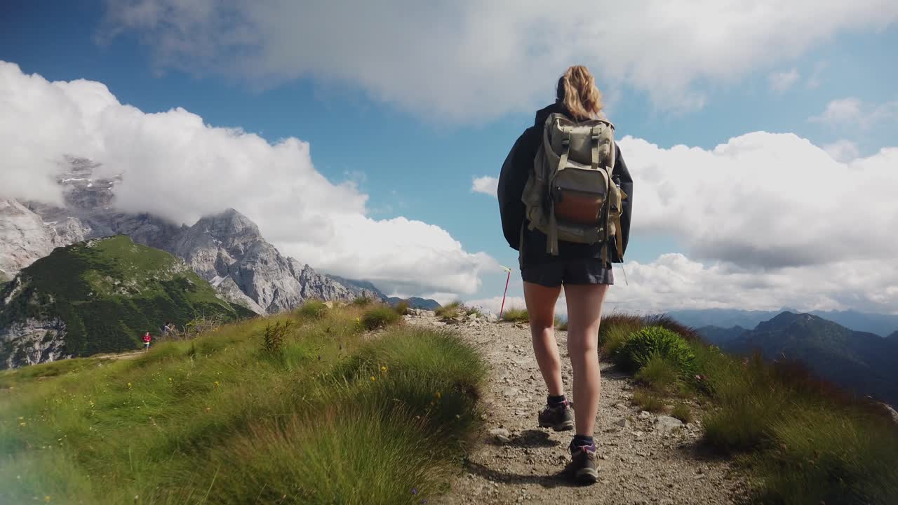 vista desde atrás de una mujer viajera turística excursionista con mochila haciendo senderismo y caminando por un sendero de montaña con los dolomitas al fondo