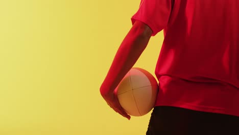 rear view of african american female rugby player with rugby ball over neon yellow lighting