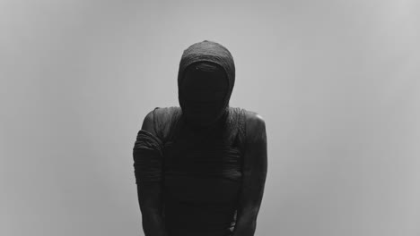 a mummy of a woman on a white backdrop slowly lowers her head