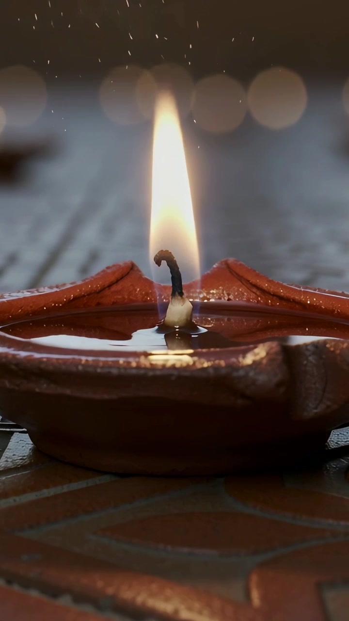 Vertical video: Sparking cotton wick fueling oil pool and diya, flame rising and sparkling on tile