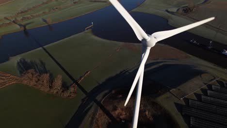 Closeup-aerial-rotating-pan-around-single-windmill-revealing-solar-panel-park-and-sustainable-industry-in-The-Netherlands-where-Dutch-river-IJssel-and-Twentekanaal-meet