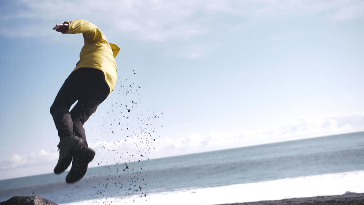 아이슬란드의 검은 해변에서 슬로우 모션으로 공중제비를 하는 젊은 여행자