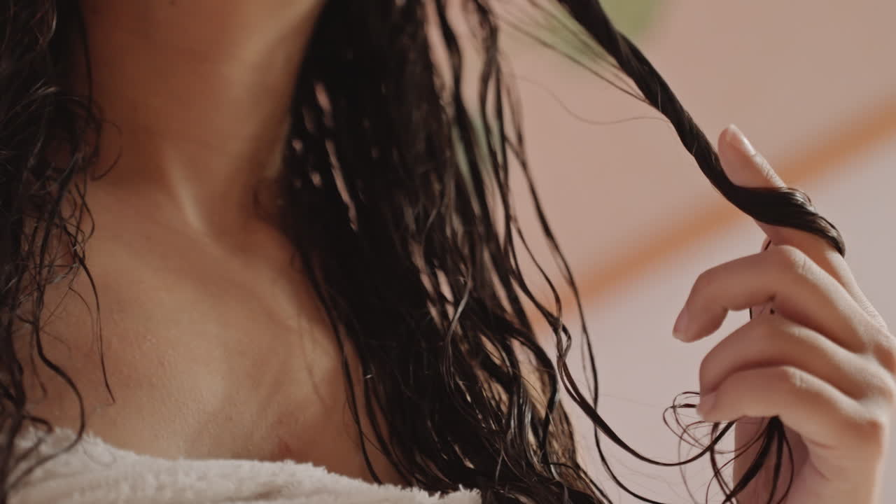 Hóspede envolta em toalha examina tranças molhadas no quarto do hotel, desfrutando de um momento de tranquilidade pós-spa. Dedos torcem e separam as mechas sob uma luz ambiente quente. Pele macia e silhueta suave, num momento de lazer e calma.
