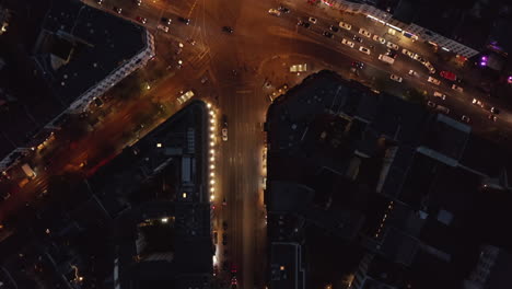 Birds-Eye-View-of-City-Street-at-Night-and-Top-View-of-Rosenthaler-Platz-Square-in-Berlin,-Germany-Mitte-distict-with-Glowing-Street-lights-and-car-traffic,-Aerial-Overhead-Shot