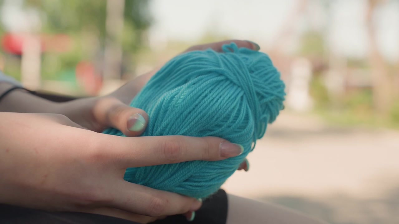 Close up of hands holding ball of turquoise yarn in soft daylight. person fingers gently manipulate textured fiber showcasing its thickness and color against outdoor background with blurred