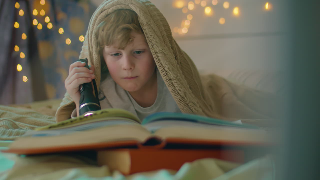 Kid Reading Book with Flashlight in Bed