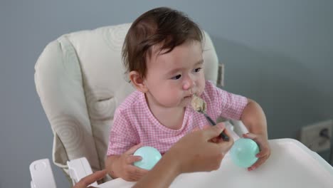 feeding the baby in her highchair while the adorable, asian toddler seems distracted, bored and uninterested