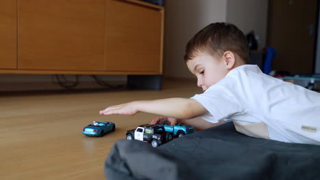 caucasian toddler lies on the plaid on the floor in the room. baby boy plays with toy cars