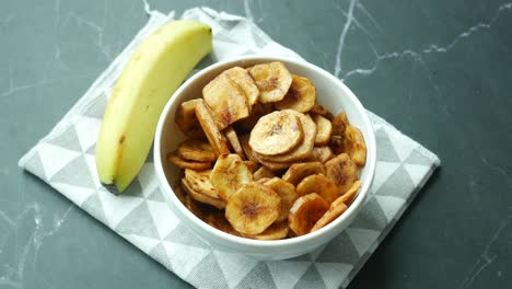 Trockene-Bananenchips-In-Einer-Schüssel-Auf-Schwarzem-Fliesenhintergrund