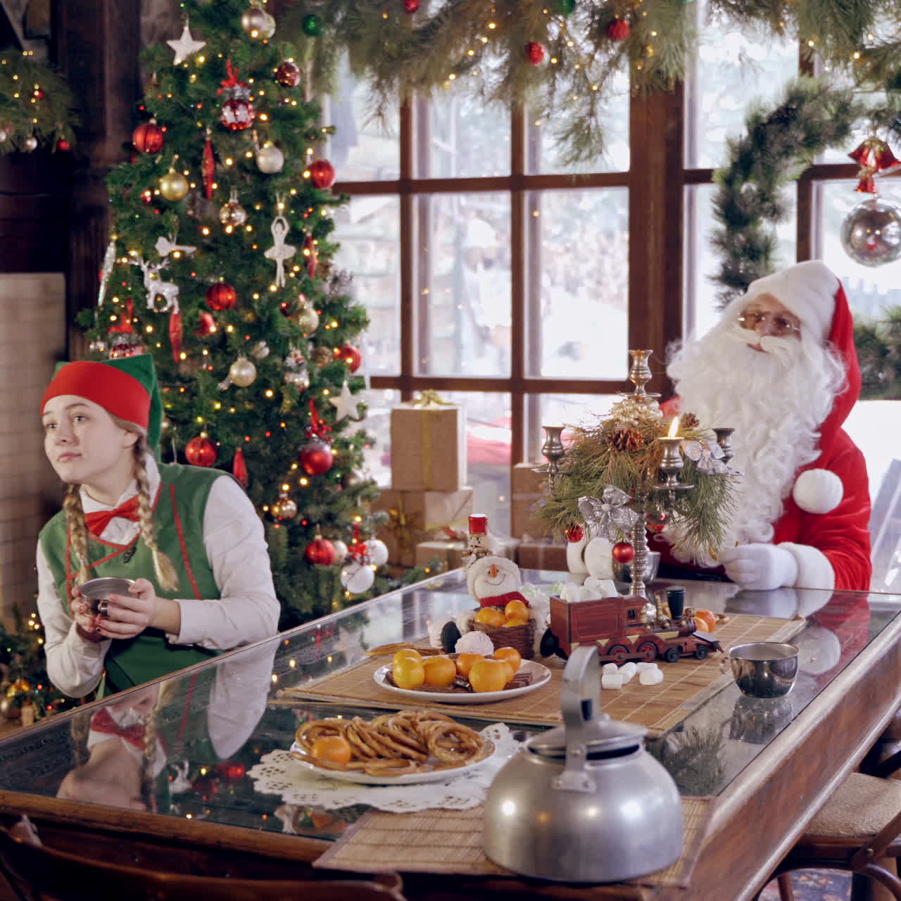 Santa Claus with elves. Cheerful elves sitting at the table together with Santa and drinking tea on Christmas background. Warm Christmas atmosphere.