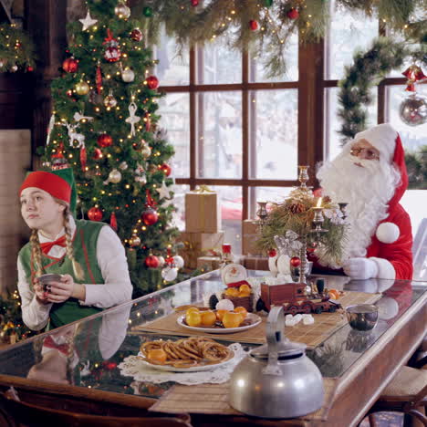 santa claus with elves. cheerful elves sitting at the table together with santa and drinking tea on christmas background. warm christmas atmosphere.