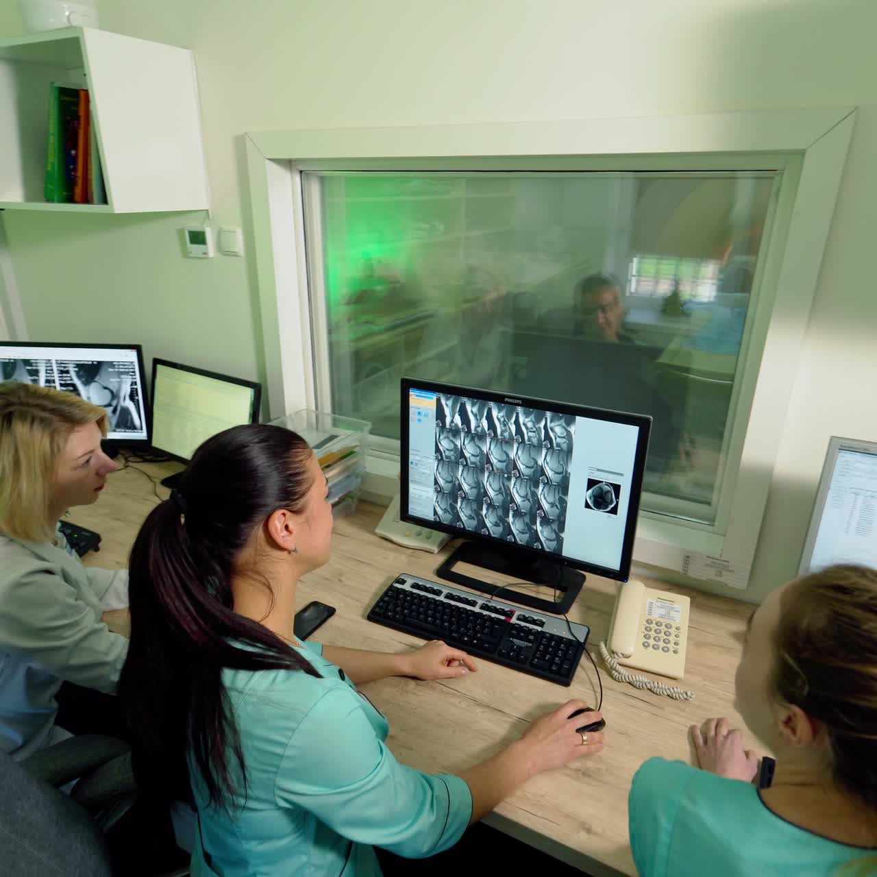 Medical workers in control room in clinic. Doctors sitting at workplace and looking at the screen of computer with a patient's x-ray shot.