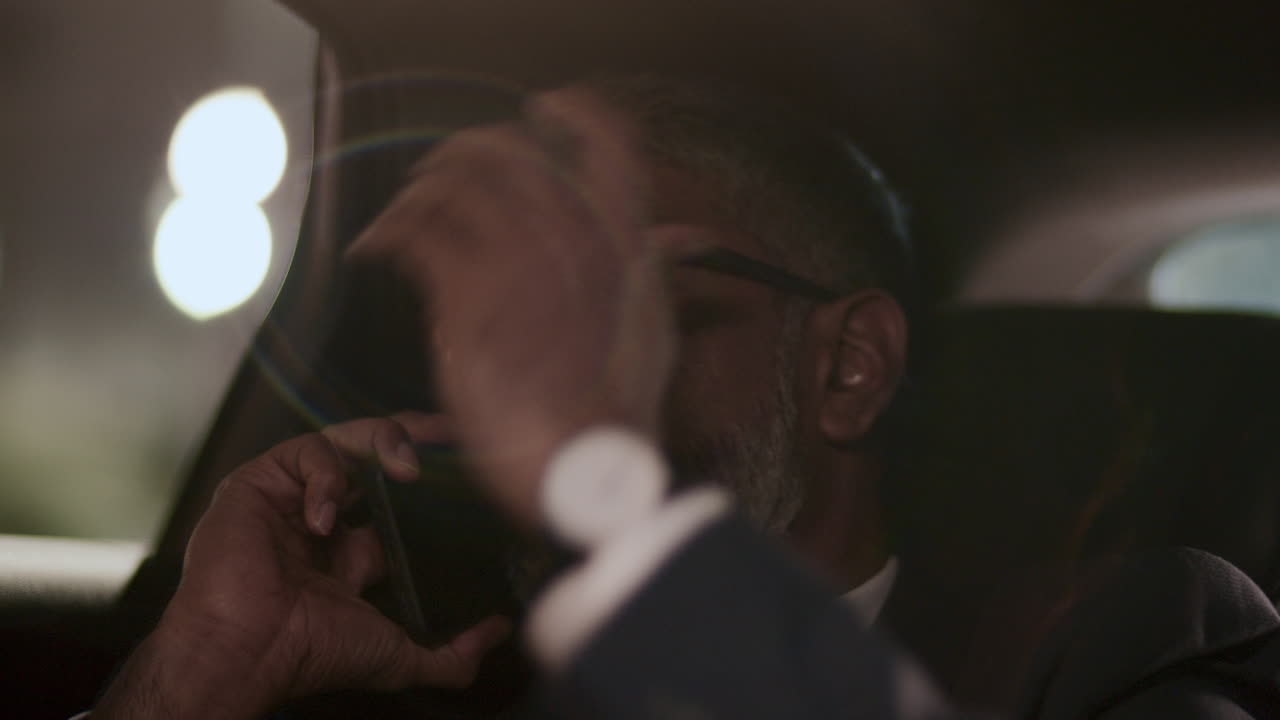 Mature Businessman Having Phone Conversation during Nighttime Taxi Ride