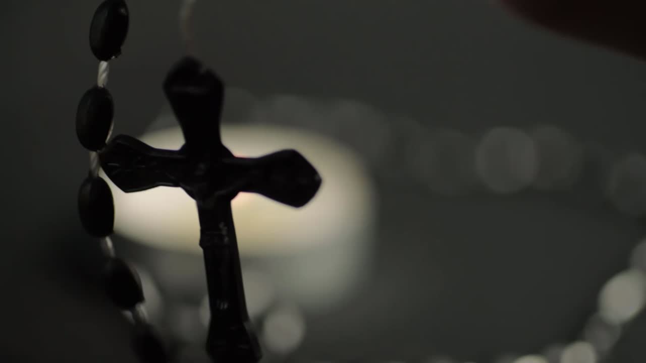 String of rosary beads and crucifix hanging in front of candle