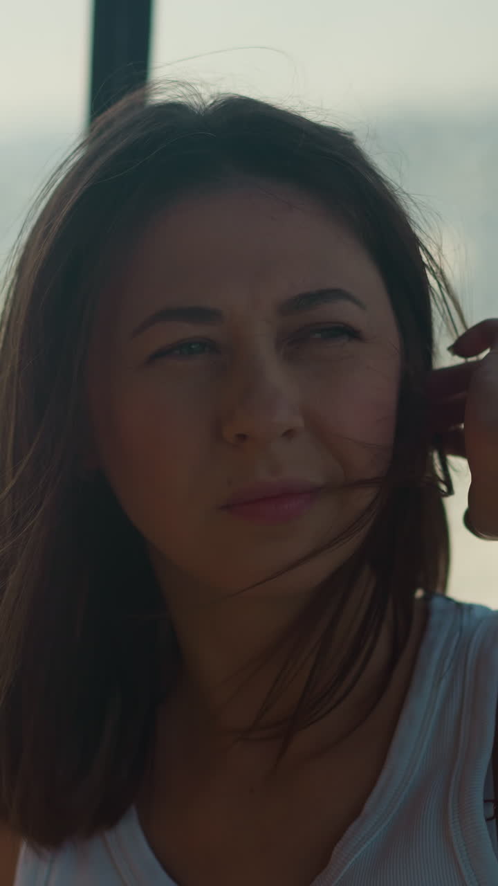 Thoughtful woman adjusts messy hair riding fast motorboat at sea resort. Lady silhouette sits in cabin of modern yacht at water trip. Passenger in boat