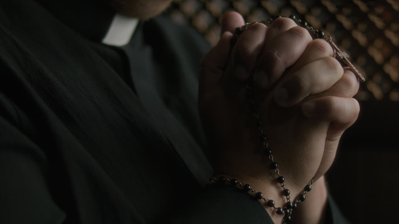 Close Up of Hands of Priest Holding Rosary in Prayer inside Confessional Booth
