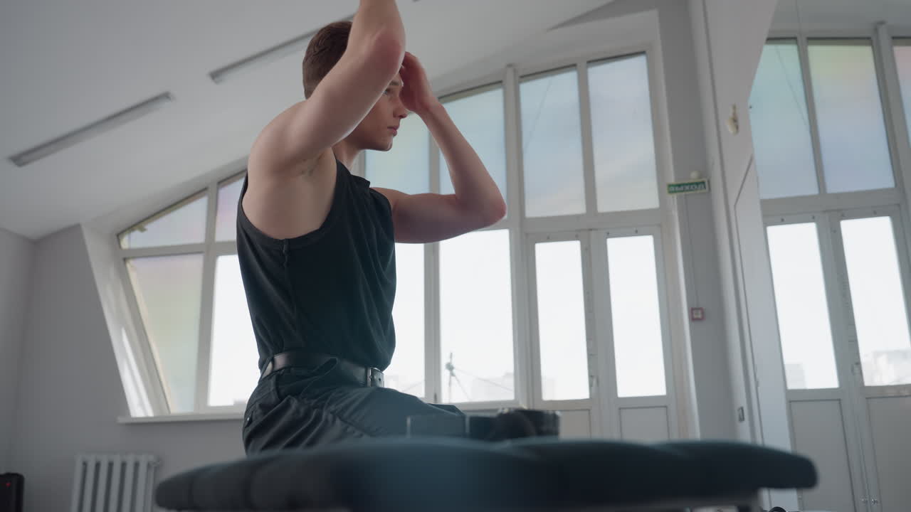 young man seated before mirror applying hair cream with gentle strokes on styled hair, bright light filtering through windows, minimalist loft studio setting
