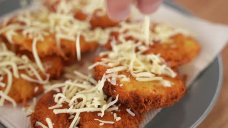 Close-up-of-sprinkling-shredded-cheese-on-top-of-fresh-hot-hash-browns,-potato-puffs