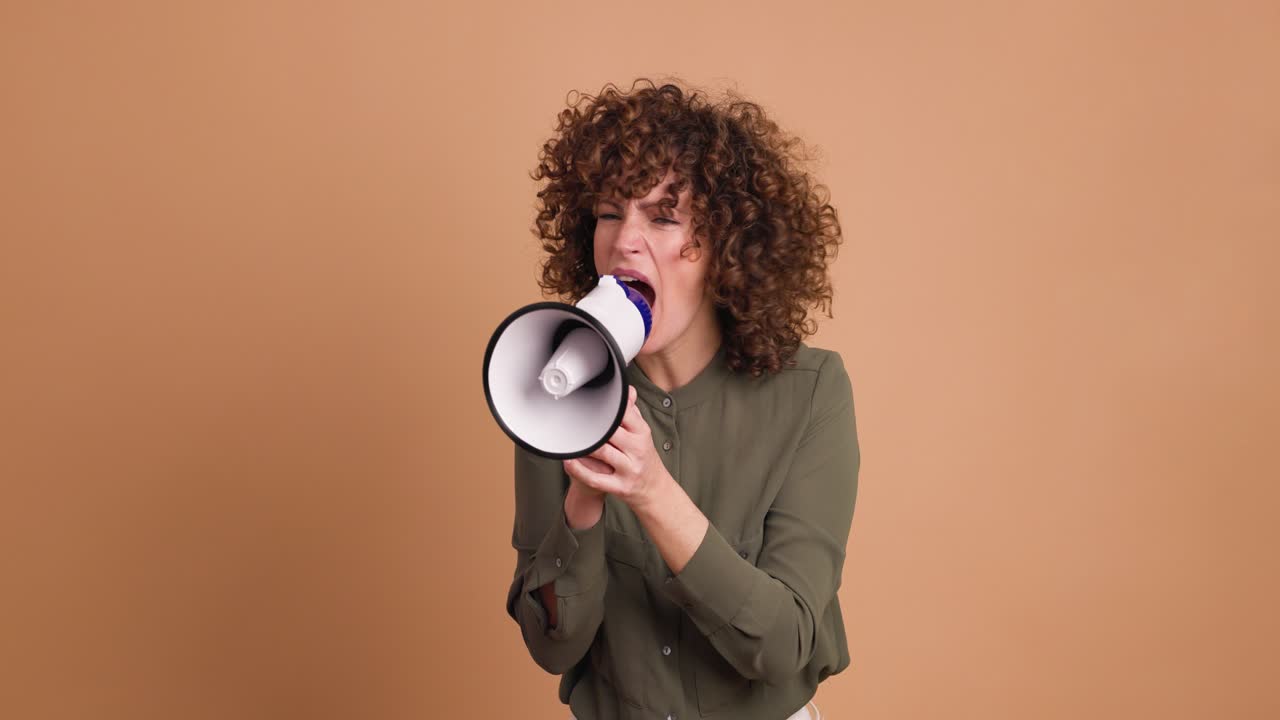 Angry adult woman screaming on loudspeaker in beige studio