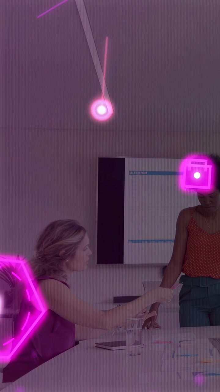 Vertical video: Left woman sliding docs to right woman, doing business as pink neon crossing frame