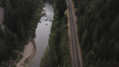 empty rural road with calm flowing river besides it, american wilderness, aerial tilt down