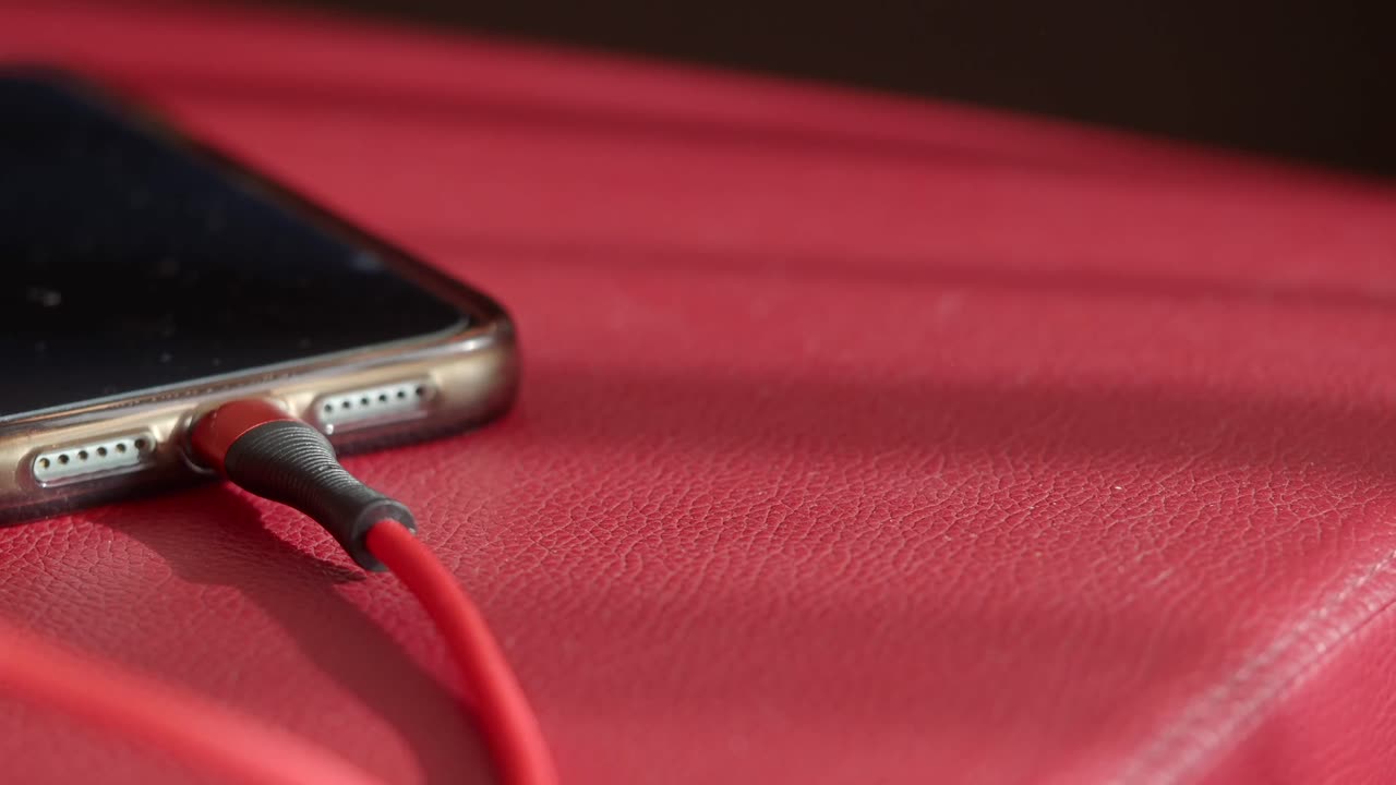 Primo piano di smartphone in carica con cavo rosso su superficie rossa.