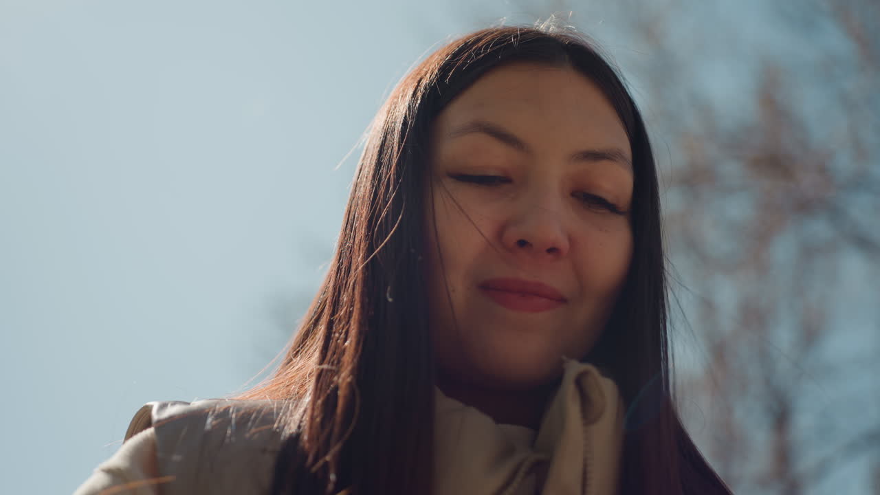 따뜻한 코트를 입은 한 여성이 야외에서 친구의 헤어스타일을 손질하는 것을 도와주며, 친구를 부드럽게 안내하는 여성, 야외의 은은한 조명 아래에서 다크 브라운 머리 여성이 친절하게 친구의 땋은 머리를 안내하고 있어요.