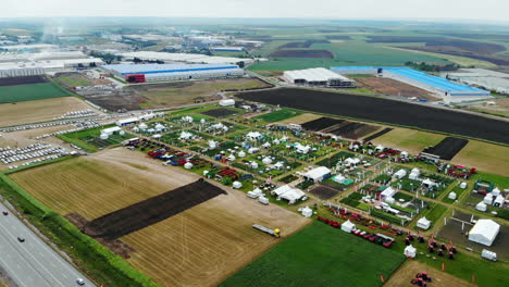 drone shot with ascending top view of agricultural expo fair on green fields of farm lands with factories and highway