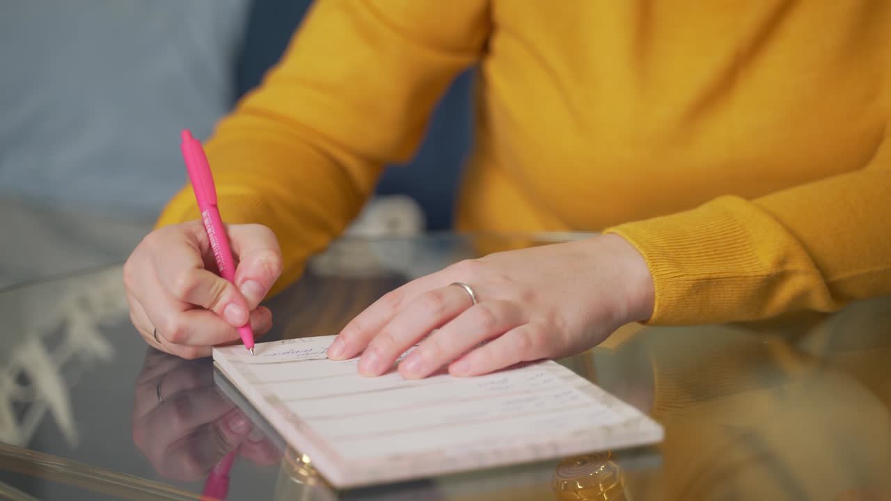 Woman is writing something on sheets of paper at glass table with pen. She reads something and corrects it with pen. Studying something, preparing for speech, checking contract, training, lecture