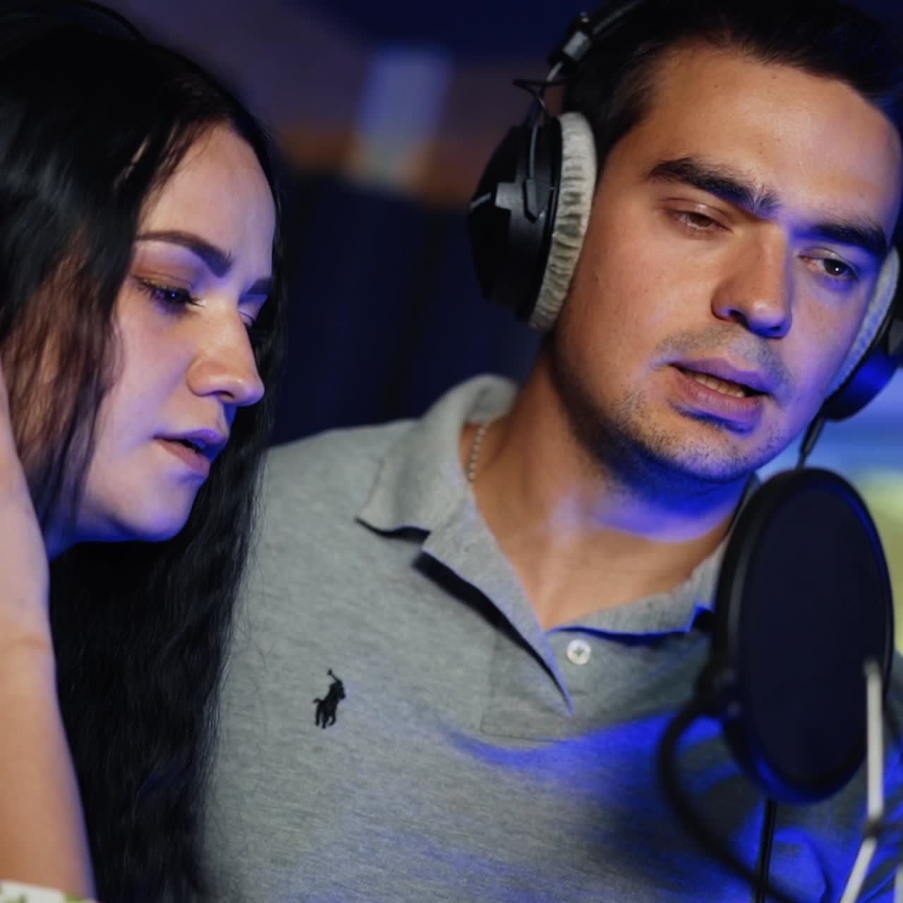 Male and female duet singing a song wearing headphones. Couple performing and recording a song in the studio