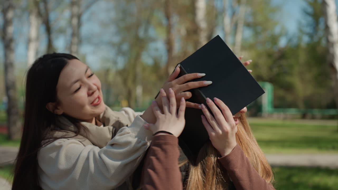 amistad a la luz del sol, interacción alegre entre una chica y una persona asiática, risas y diversión entre amigos bajo abedules, instantánea de amistad alegre con gestos divertidos en un parque iluminado por el sol