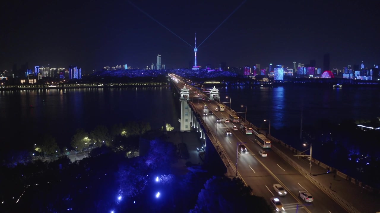 Vista aerea mozzafiato del traffico che scorre sul Ponte del Fiume Yangtze verso l'illuminata Torre della TV di Tortoise Mountain e lo skyline della città sotto spettacoli di luci blu a Wuhan, Cina, di notte.