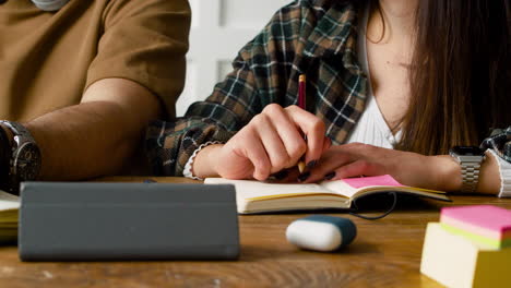 close up view of hands of a student holding pen and gesturing sitting at table