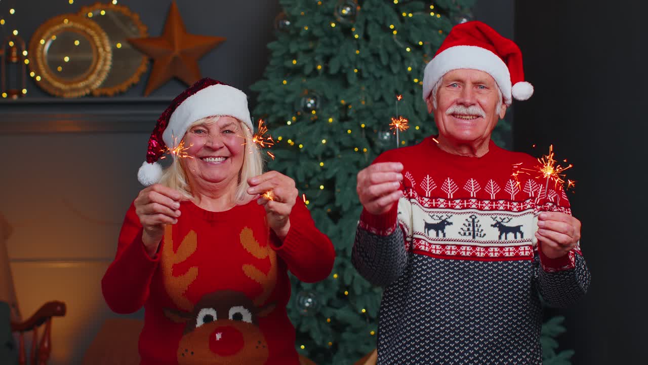 una pareja de ancianos en suéteres festivos con luces de bengala disfrutando de la víspera de navidad en la habitación de casa