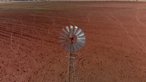dolly inverso aéreo que revela una bomba de viento en funcionamiento en una granja con tierra arada sin usar