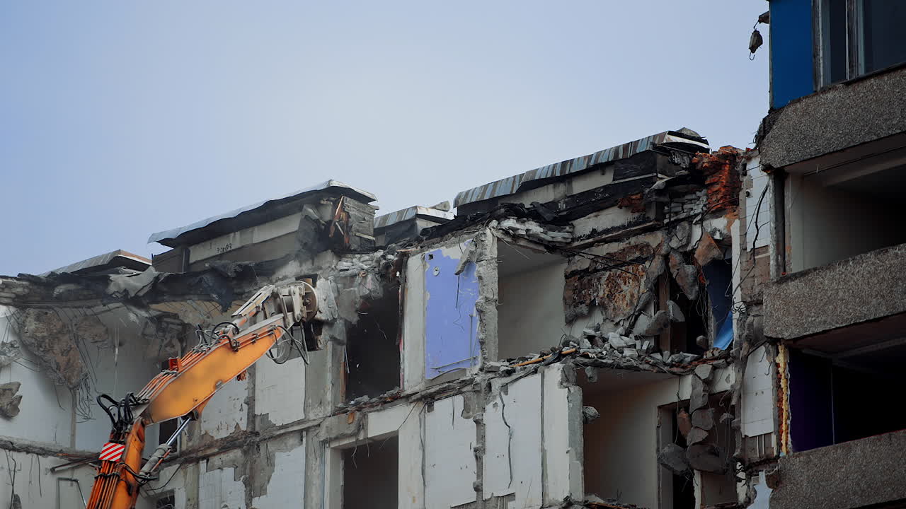 Dismantling the upper floors of the multi-storey building. Crushing the floors of the high house. Excavator work in the deconstruction site.