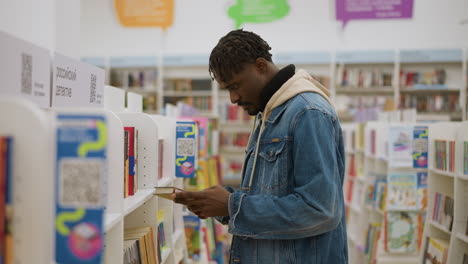 confident young man in denim jacket standing in library, looking at bookshelves, focused on selecting books in well-organized space, embodying calm, thoughtful moment in study environment