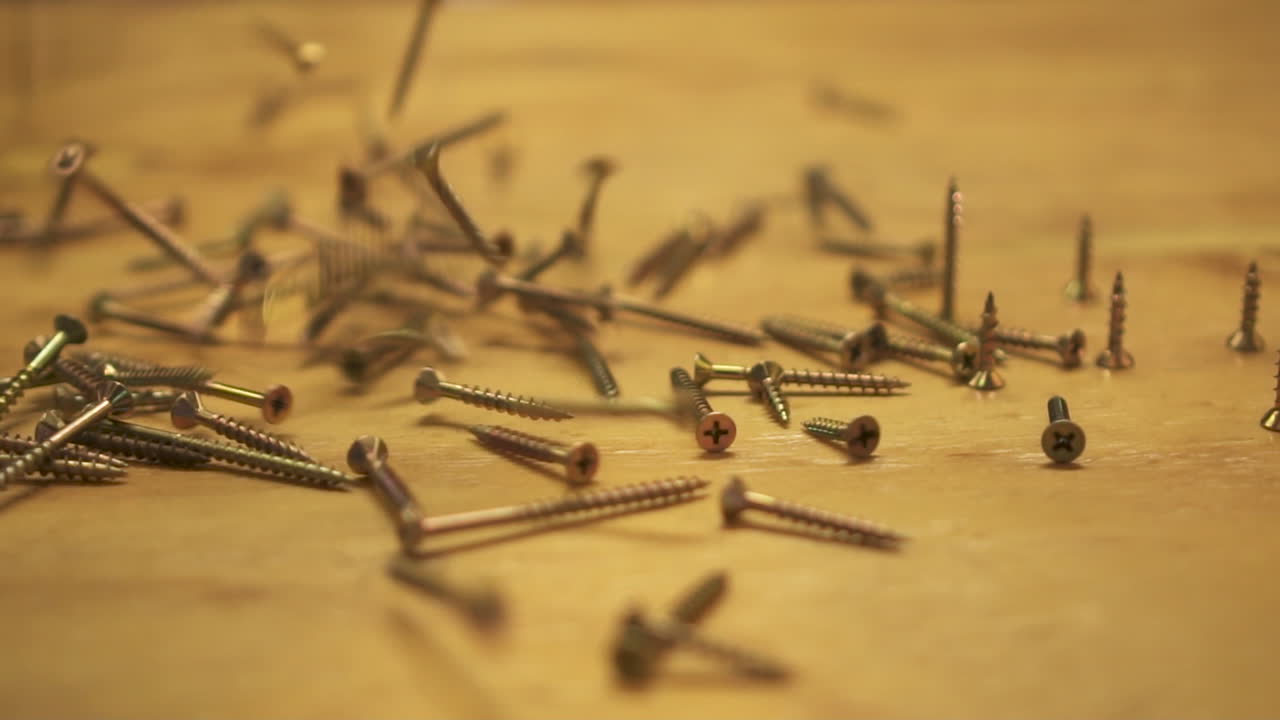 Slow motion of hundreds of screws falling on wooden table, slide right, close up