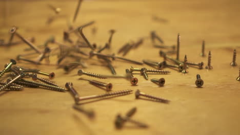 slow motion of hundreds of screws falling on wooden table, slide right, close up