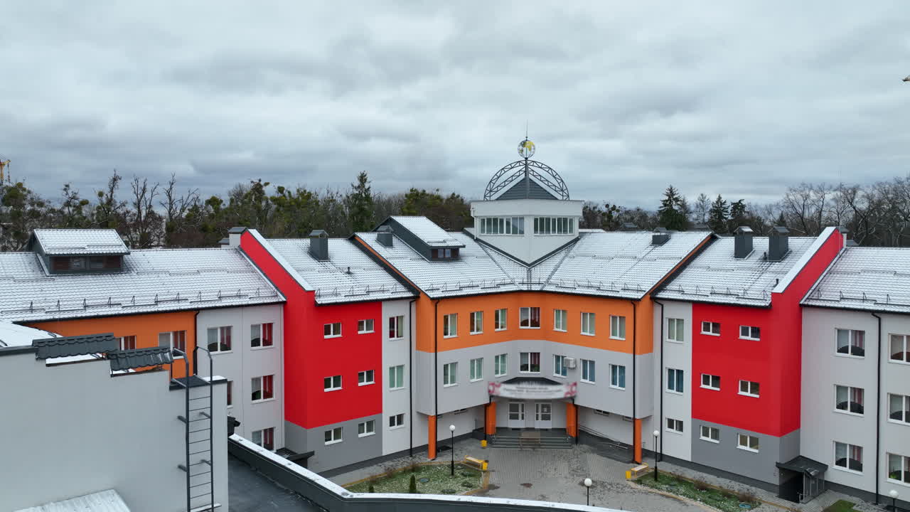 Newly-built bright building in the new residential area. Flight above the three-storied house. Winter park and cloudy sky at the backdrop.