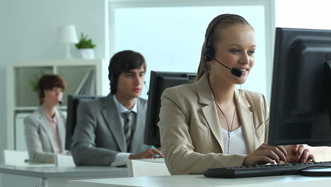 telemarketer office, in the foreground a blonde woman talking with a headset and typing on the computer keyboard