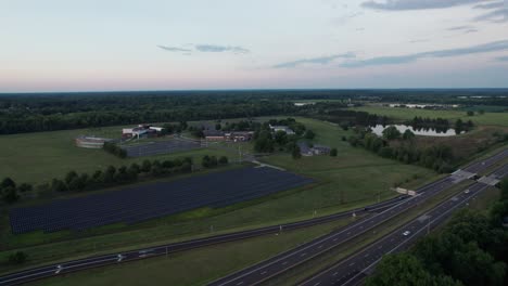 Drone-hovering-above-the-busy-road-with-solar-panel-built-in-its-sideway-and-a-nearby-town-surrounding-trees