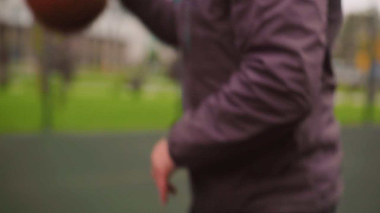 white man dribbling basketball outdoor court, wearing beanie and headphones, focused low stance and quick footwork, blue sneakers striking wet asphalt, urban apartment buildings blurred in background