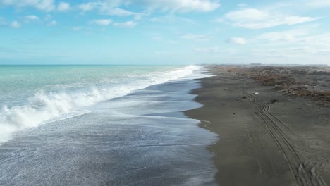 Low-aerial-above-white-water-and-sea-spray-at-vast-Kaitorete-Spit-with-turquoise-colored-South-Pacific-Ocean