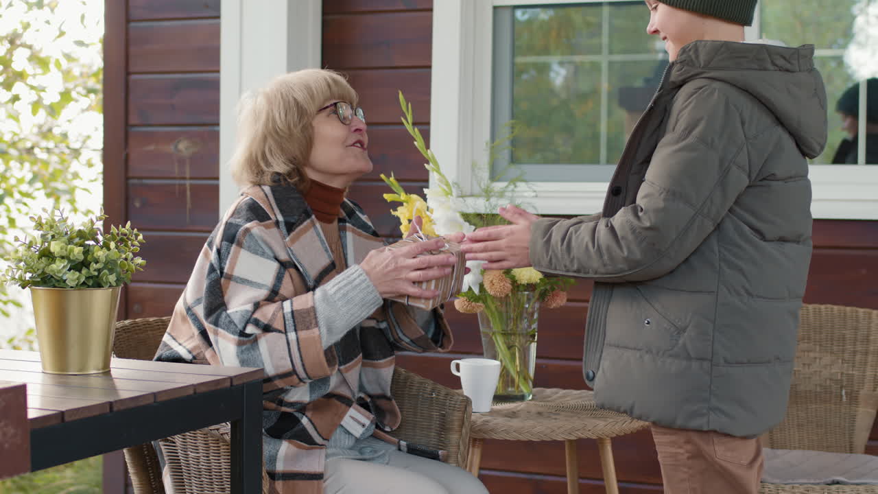 Kid Bringing Present to Granny Sitting on Terrace