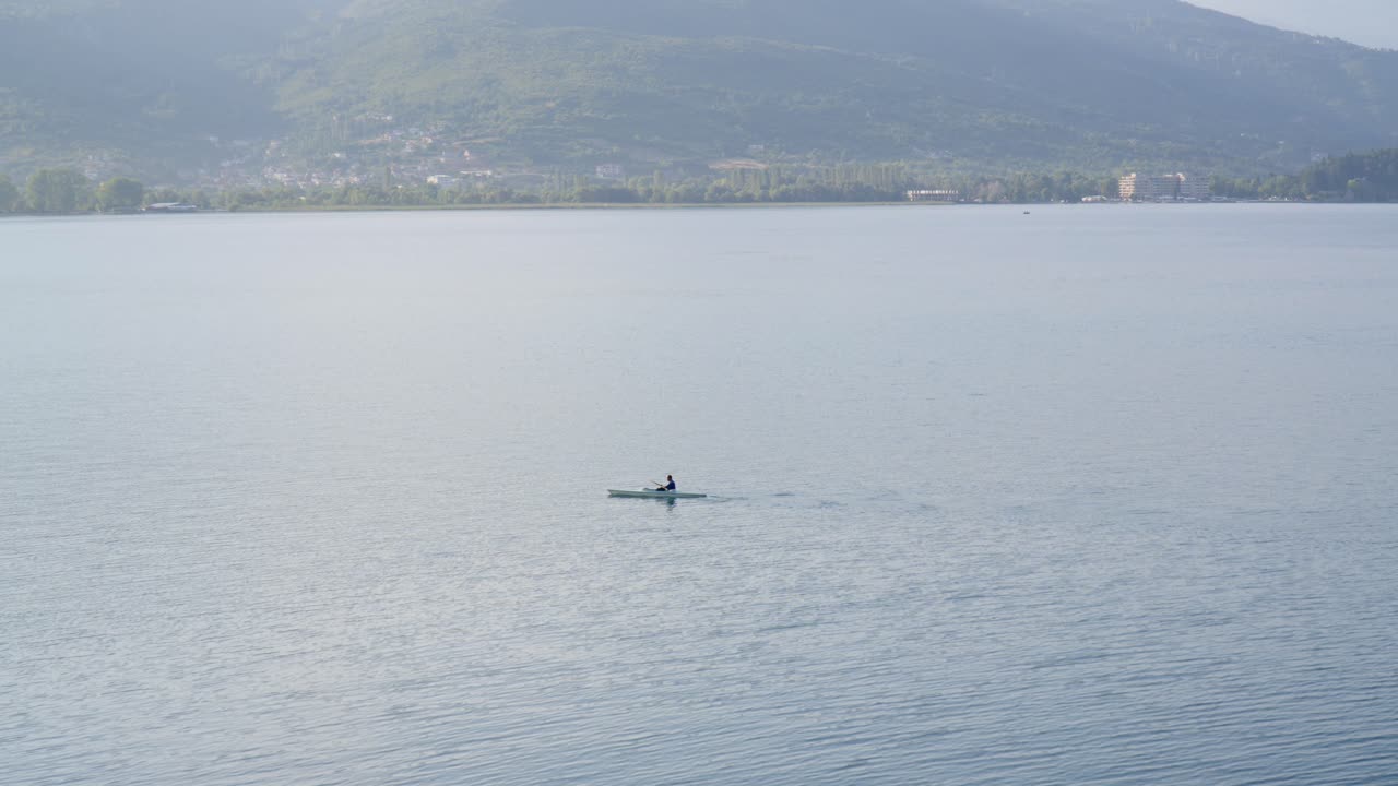 A single kayaker paddles across lake Ohrid, high angle view with mountains in background