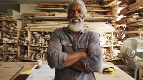 Portrait-of-african-american-male-carpenter-with-arms-crossed-smiling-in-a-carpentry-shop