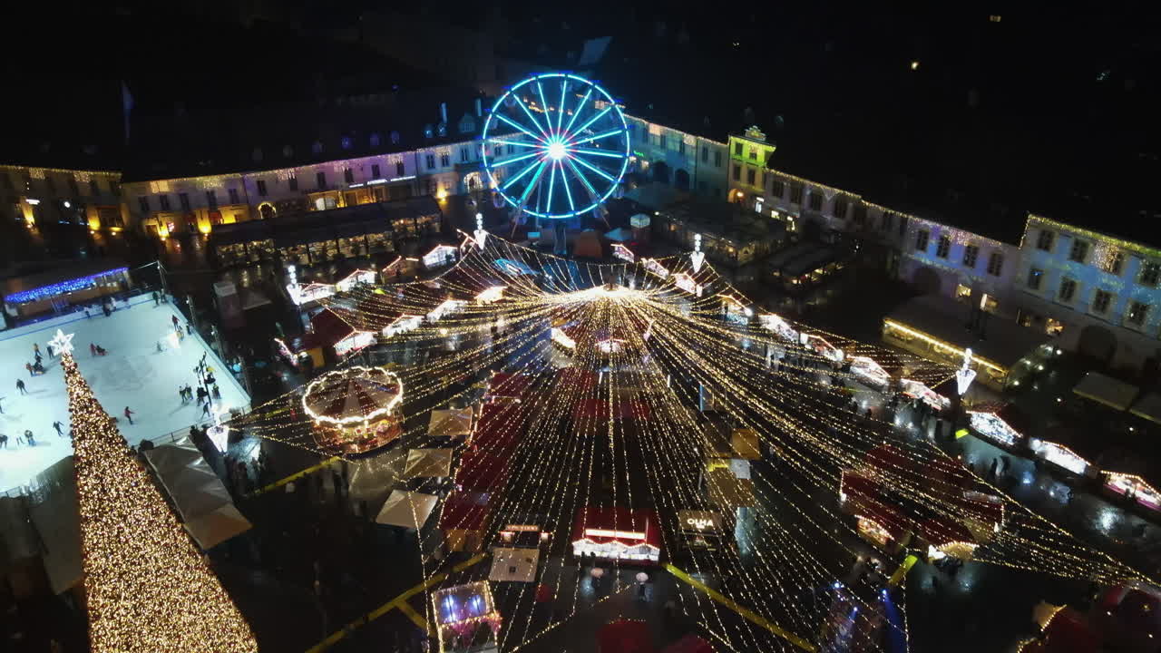 Aerial drone view of The Big Square in Sibiu at night, Romania. Old city centre decorated for Christmas. Ferris wheel, skating rink, old traditional buildings, people
