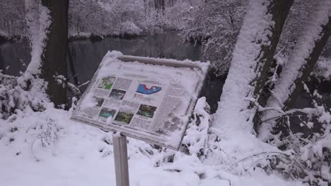 Schneebedeckte-Informationstafel-Mit-Blick-Auf-Das-Naturschutzgebiet-Niebieskie-Zrodla,-Waldfluss,-Zurückziehen