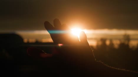 man moving right hand in front of sunrise, silhouette, anamorphic flares